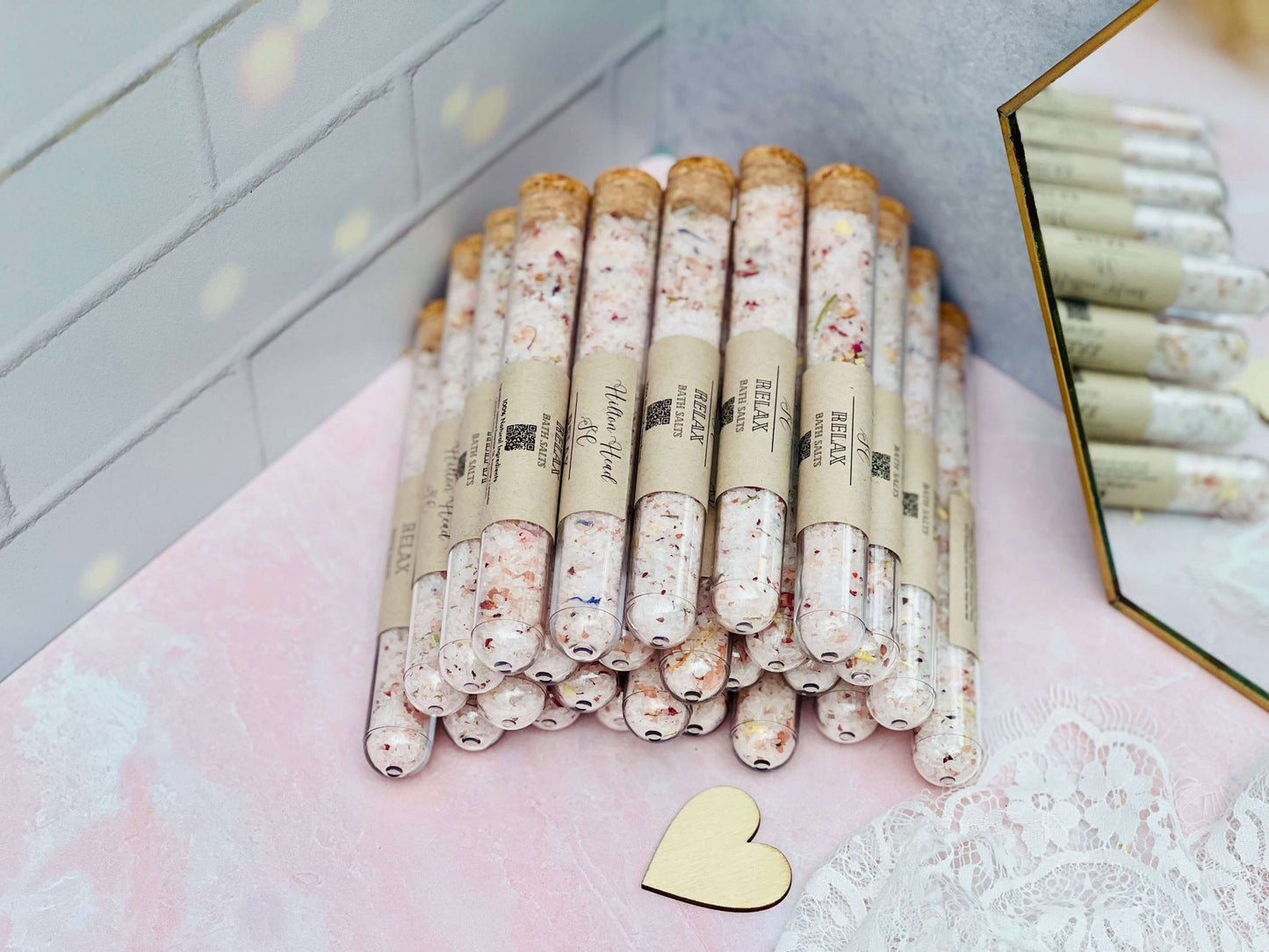 Stack of mixed bath salts in glass tubes with natural ingredients, displayed on a pastel backdrop with a heart accent.