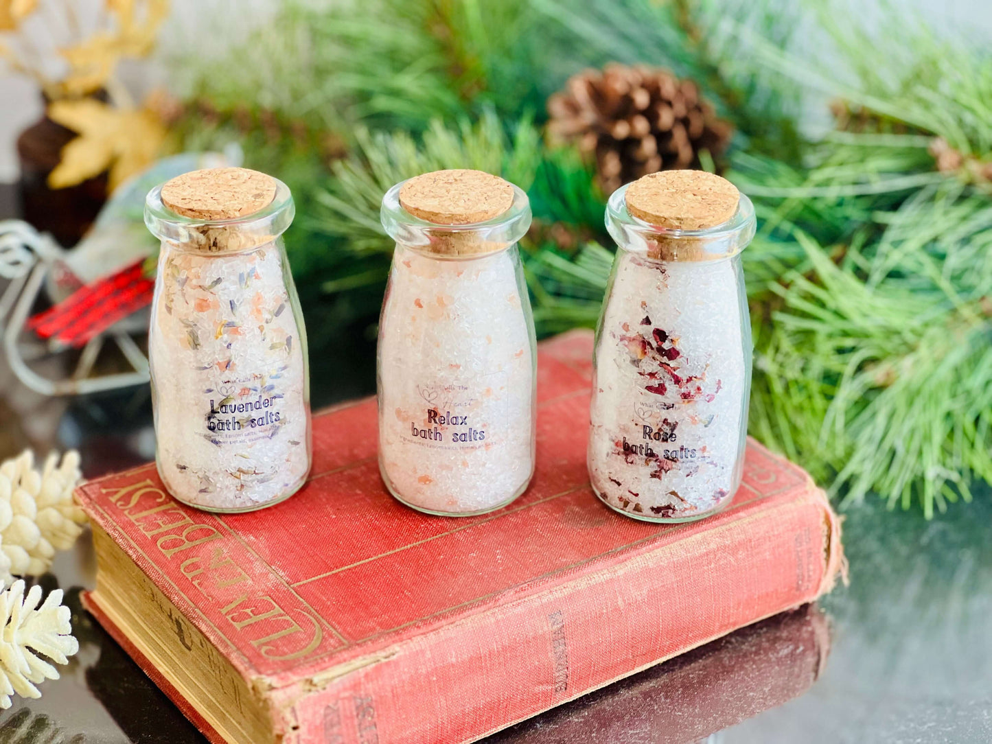 Handcrafted bath salts in glass jars with cork stoppers: Lavender, Rose, and Unscented varieties on a vintage book.