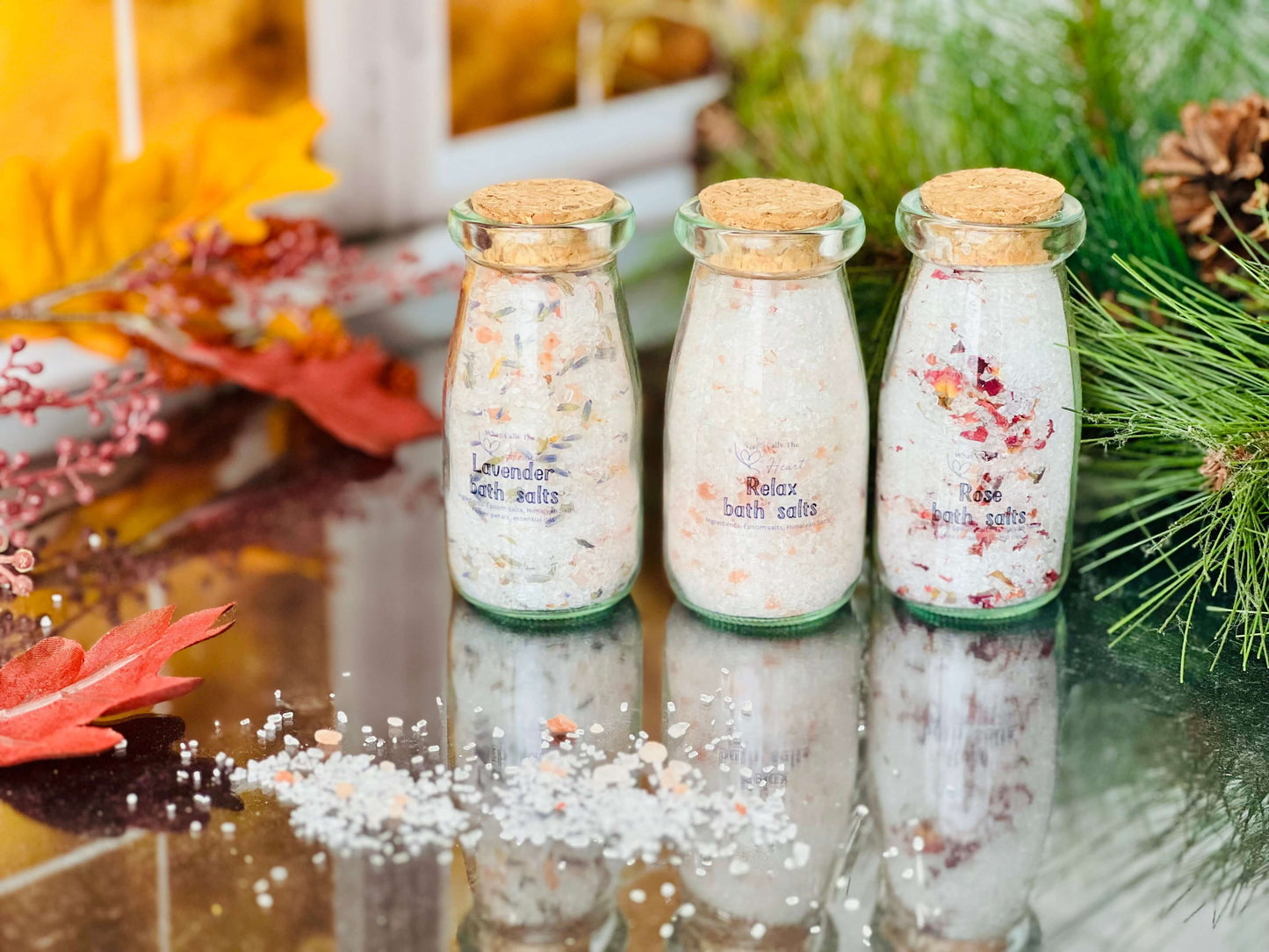 Three handcrafted bath salts jars with cork stoppers: Lavender, Rose, and Unscented, arranged with autumn leaves.