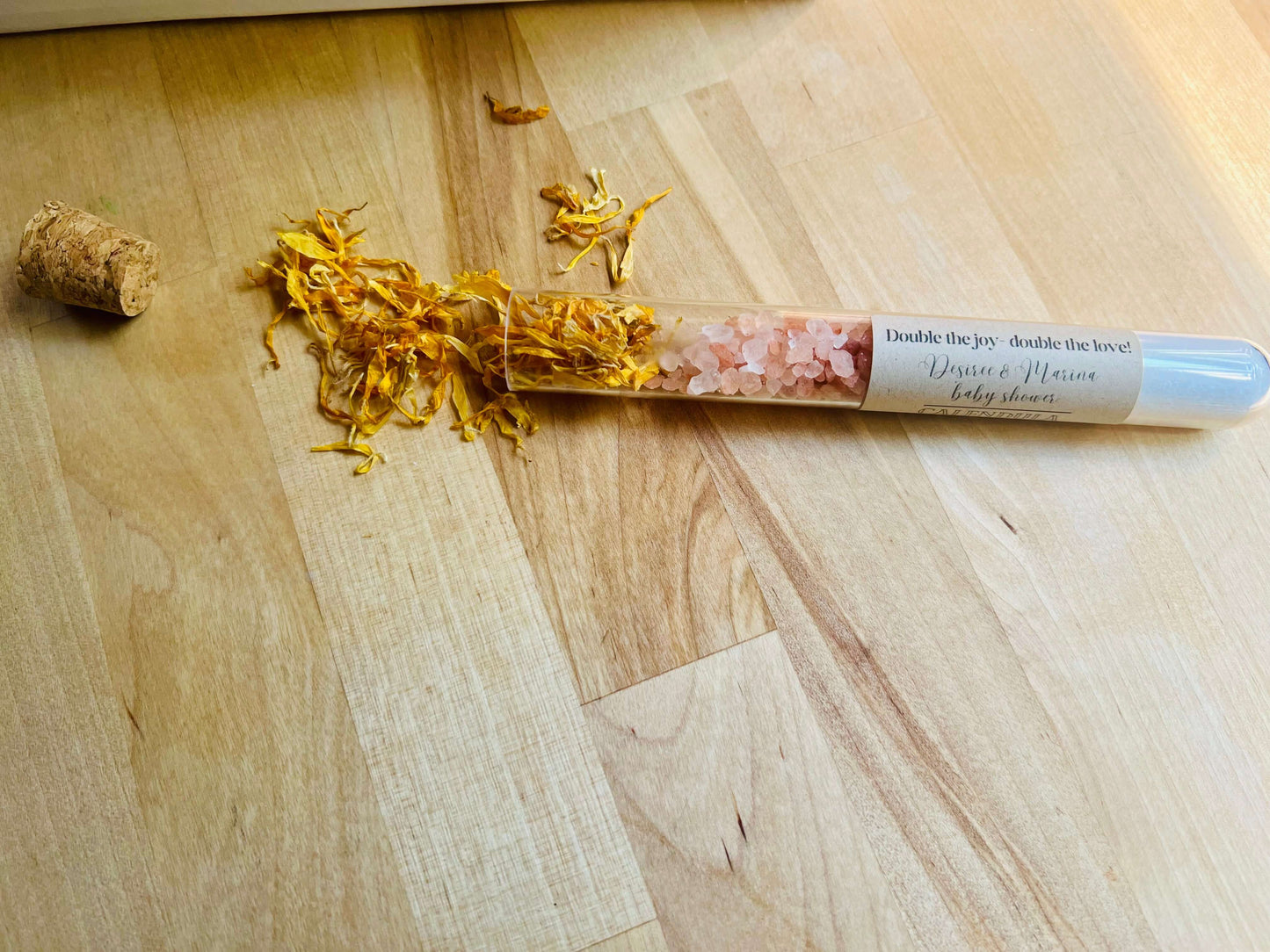 Calendula bath salts with pink Himalayan salt, spilling from a test tube onto a wooden surface.