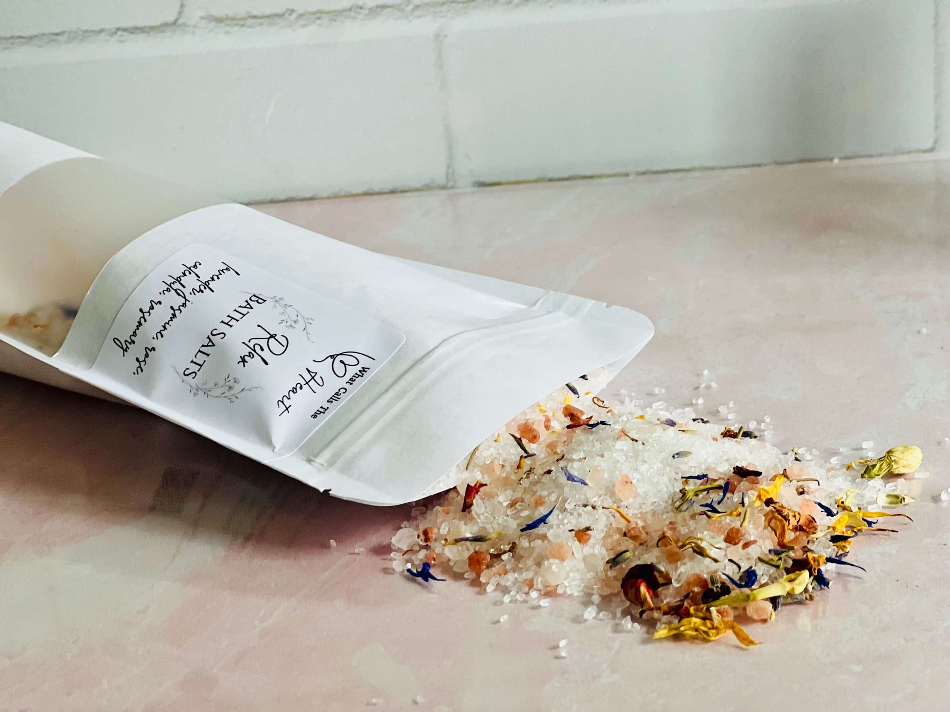 Handmade bath salts with natural ingredients spilling from a pouch, featuring Himalayan pink salt and dried flowers.