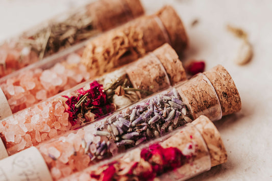 Variety pack bath salts in glass tubes with cork lids, featuring pink Himalayan salt, flowers, and herbs for relaxation.
