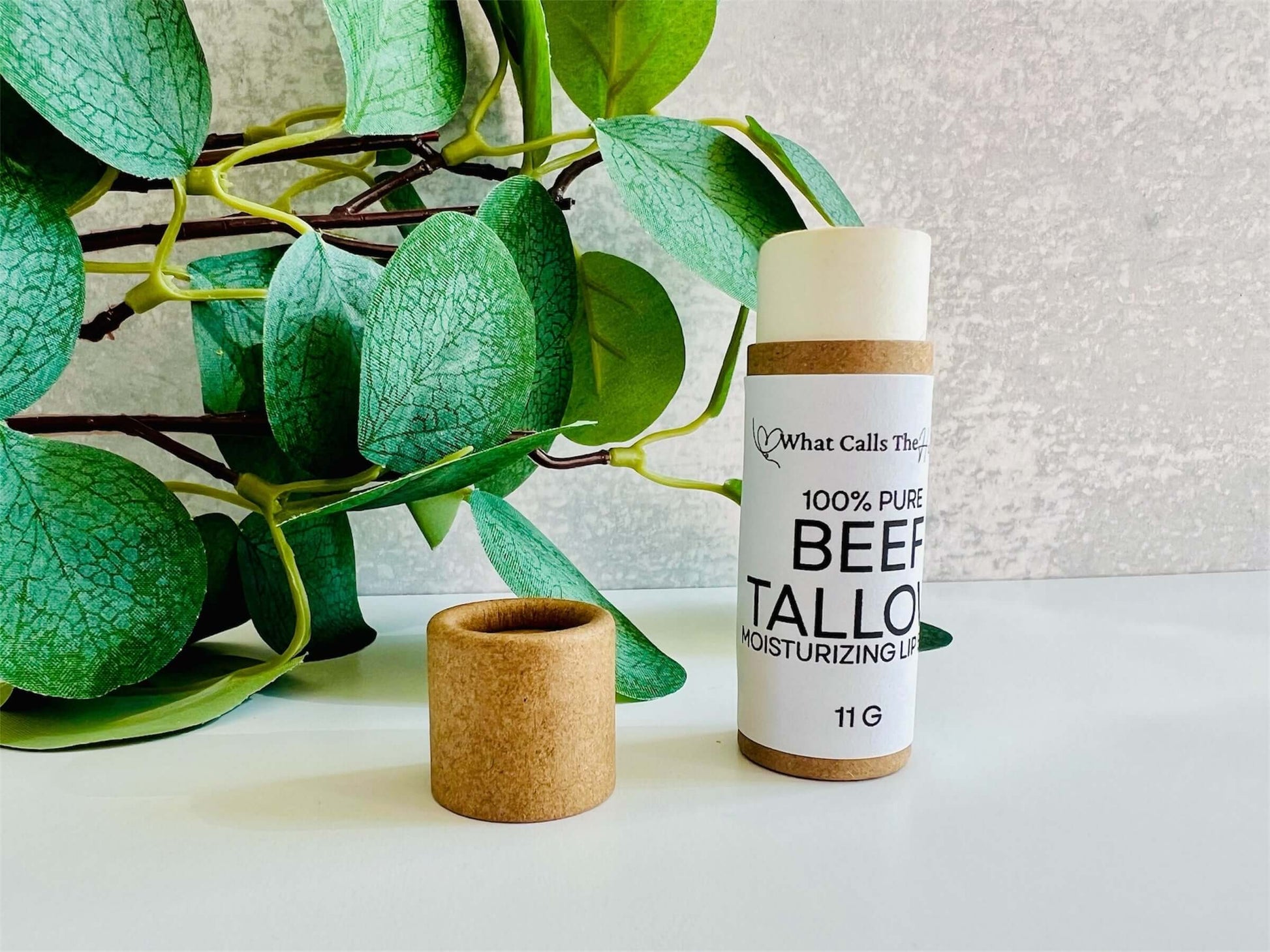 Beef tallow organic lip balm in a biodegradable tube, surrounded by green leaves, emphasizing natural skincare.